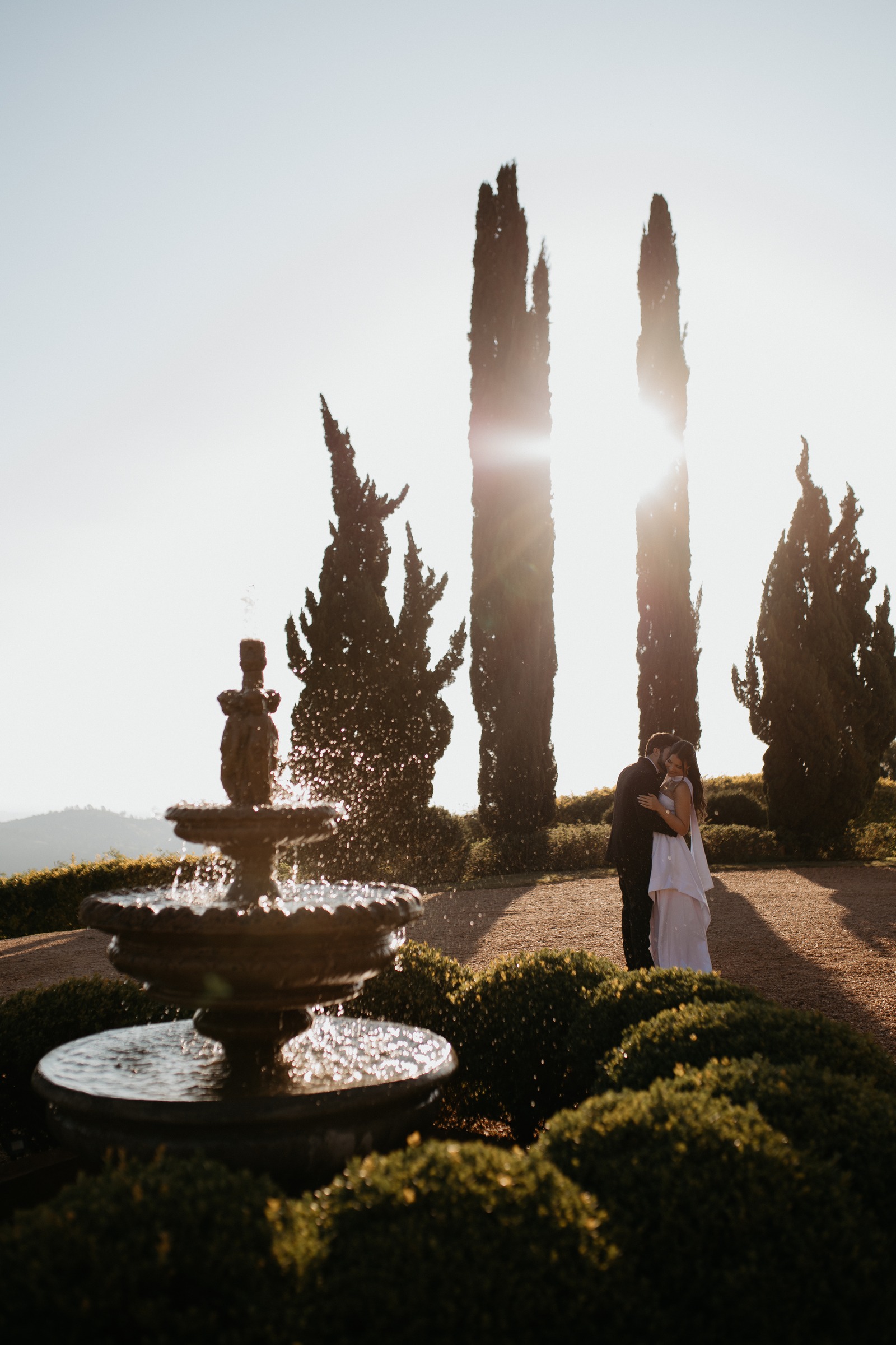 Casal em um jardim com ciprestes iluminados pelo sol